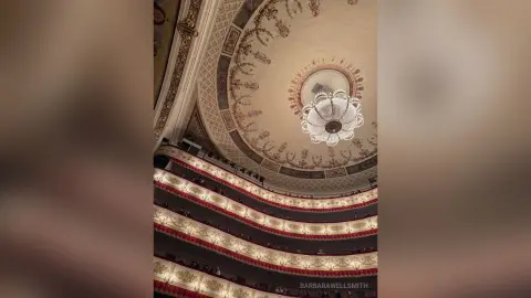 Ornate gold ceiling and crystal chandelier in a grand, luxurious classical opera house theater.