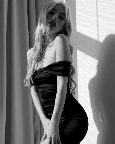 Elegant blonde woman in a black satin cocktail dress posing in soft sunlight for a moody black and white portrait.