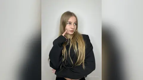 Blonde woman in a black long-sleeve shirt posing thoughtfully against a white background.
