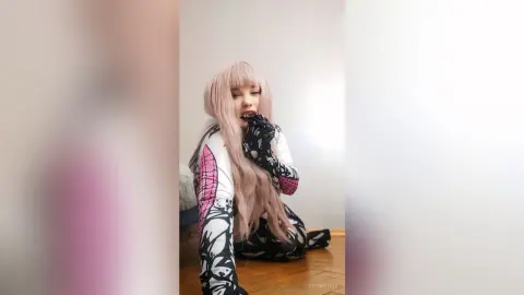 EstherTrix with long pink hair poses in a black and white patterned outfit while looking at the camera.