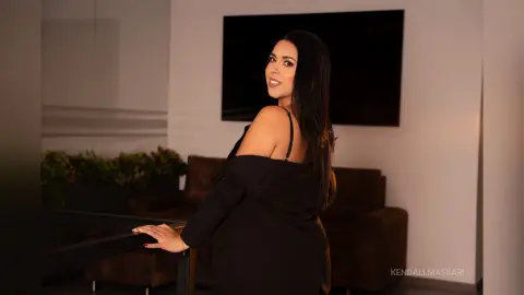 Elegant woman in a black off-the-shoulder dress posing in a modern living room with a sophisticated mood.