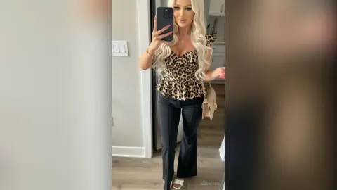 AlexaEvans poses in a mirror wearing a leopard print peplum top and black flared pants, showing off her long blonde hair and gold jewelry.