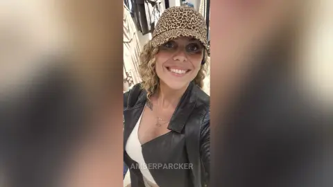 Smiling woman in a black leather jacket and leopard print cap posing in a clothing boutique.