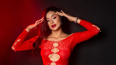 Glamorous woman in a red lace cutout bodysuit posing against a moody red and black studio background.