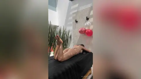 Relaxed woman in a bikini sunbathing on a black lounge bed in a bright, minimalist modern room.