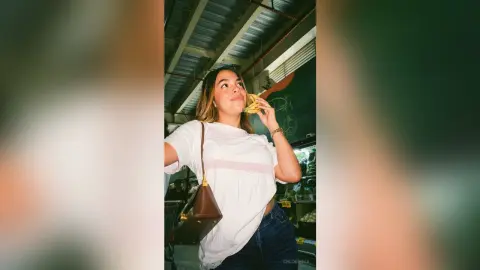 Smiling young woman in a white t-shirt eating a snack in a grocery store setting.