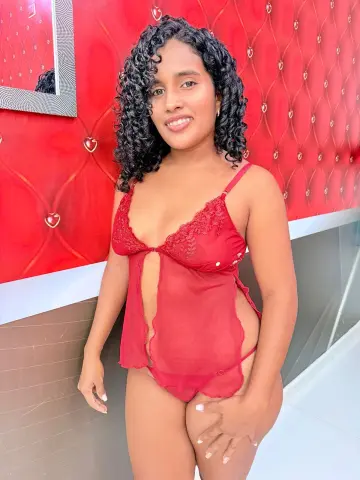 Smiling woman in red lace lingerie posing against a vibrant red tufted wall background.