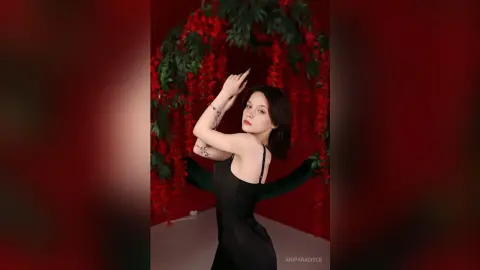 Elegant woman in a black slip dress posing against a romantic red floral backdrop.