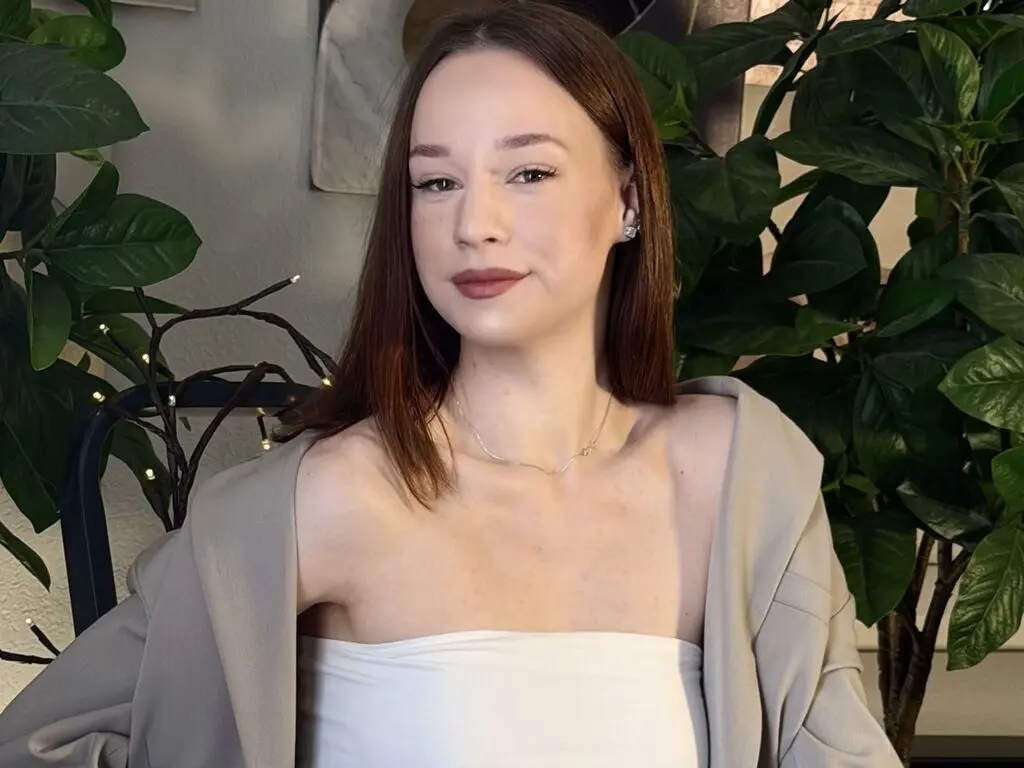 Young woman in a white tube top and beige cardigan sitting in a bright room with green plants.