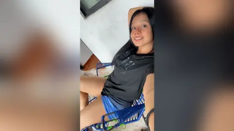 Smiling young woman in a black t-shirt and blue shorts relaxing on a blue chair in a bright room.