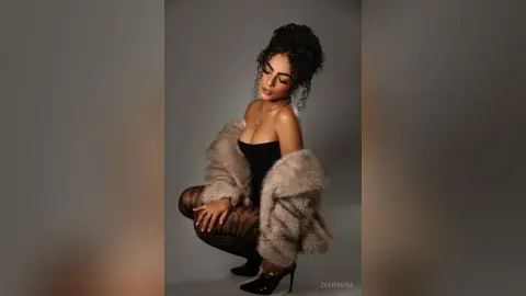 Elegant woman in a black bodysuit and faux fur coat posing glamorously against a neutral studio background.