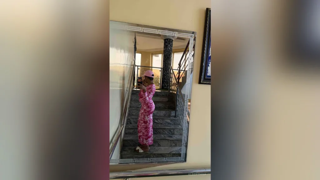 AlbertNina — AlbertNina takes a mirror selfie wearing a pink floral patterned dress and a pink cap while standing on a staircase.