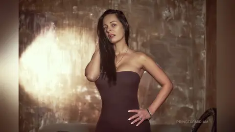 Elegant woman in a dark strapless dress posing against a textured golden background in soft cinematic lighting.