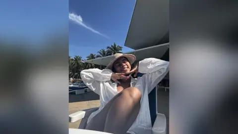 Smiling woman in a white linen shirt and sun hat relaxing outdoors on a sunny summer day.