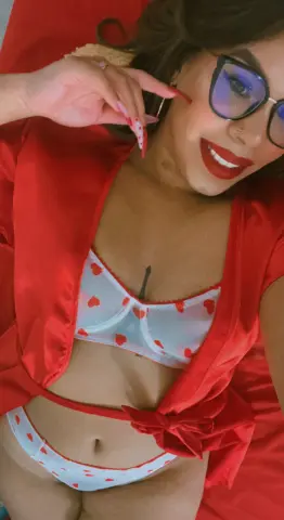 Smiling woman in red robe and white heart print lingerie relaxing in a cozy setting.