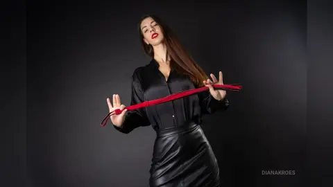 Elegant woman in a black silk blouse and leather skirt holding a red ribbon against a dark studio background.