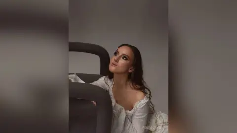 Dreamy portrait of a woman in a white ruffled blouse looking upward in a minimalist studio setting.