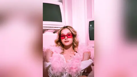 Trendy woman in pink sunglasses and a fluffy pink outfit posing in a retro pink-lit room with vintage TVs.