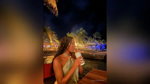 Young woman in a green halter top sipping a drink at a tropical beach resort at night.