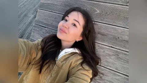 Young woman in a tan corduroy jacket relaxing on a wooden deck under soft natural light.