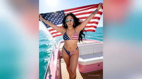 Woman in American flag bikini holding US flag on a sunny boat trip in the turquoise ocean.