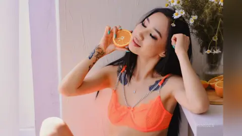 Young woman in orange lace lingerie holding an orange slice in a bright, airy indoor setting.