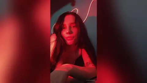 Young woman with long dark hair posing under moody red neon lighting in a dark room.