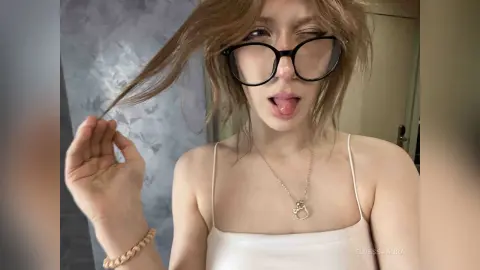 Playful young woman with glasses and white camisole posing in a modern indoor setting.