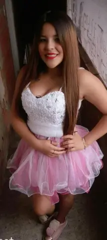 Smiling young woman in a white lace top and pink tulle tutu skirt posing in a rustic doorway.