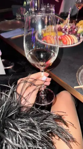 Person in a black feathered outfit holding a glass of red wine at an elegant evening party.
