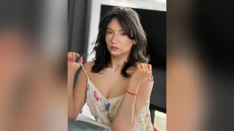 MnemoZeina poses in a white floral camisole, looking at the camera with her dark hair down.