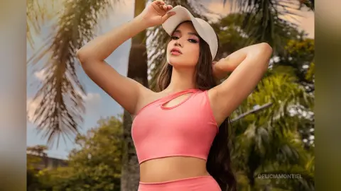 Young woman in a pink crop top and white sun hat posing in a tropical palm tree garden.