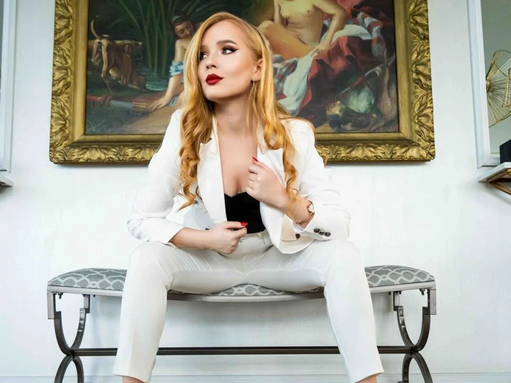 ChloeRichardson sits on a bench wearing a white suit and black top with her blonde hair flowing over her shoulders.