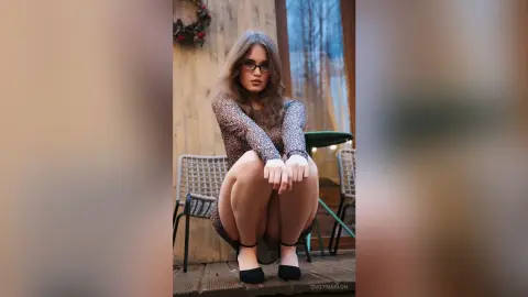 Young woman in a leopard print dress and glasses sitting on a patio chair in a cozy outdoor setting.