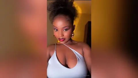 Valjohn poses in a white low-cut top, showing off her cleavage and red lipstick with her hair styled up.