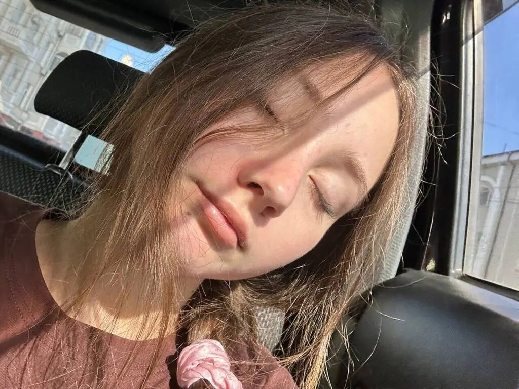 Young woman with long brown hair sleeping peacefully in a car seat under warm sunlight.