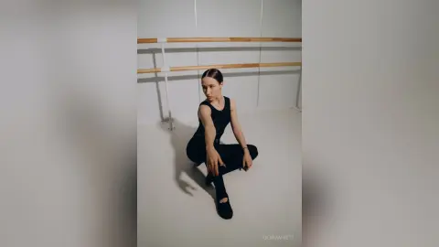 Athletic woman in black bodysuit posing in a minimalist dance studio with ballet barres.