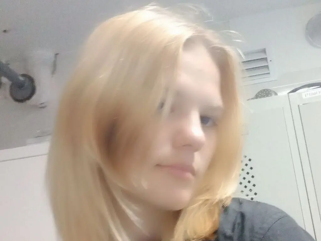 Blonde woman in a black shirt posing in a bright indoor setting with a soft, natural mood.