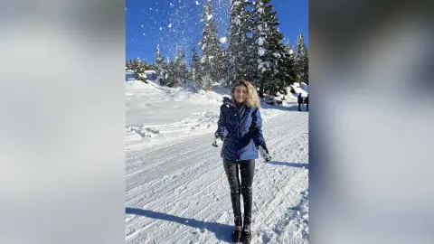 Happy woman in blue winter jacket playing in the snow at a sunny mountain ski resort.