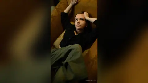Melancholic young woman in a black shirt and olive trousers relaxing on a vintage yellow sofa.
