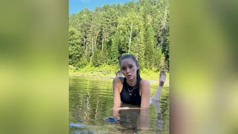 Young woman in a black tank top relaxing in a calm forest lake during a peaceful summer day.