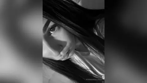 Close-up black and white portrait of a young woman with long dark hair looking thoughtfully into the camera.