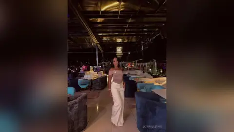 Elegant woman in a white jumpsuit standing in a modern, dimly lit upscale lounge at night.