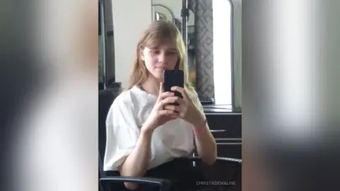 Young woman in a white t-shirt taking a casual mirror selfie in a bright, modern room.