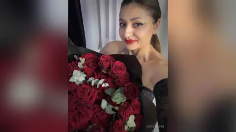 Elegant woman in a black lace dress holding a large bouquet of red roses in a romantic setting.