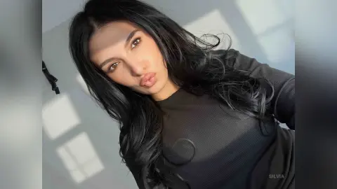 Young woman with long dark hair wearing a black ribbed top in bright sunlight.