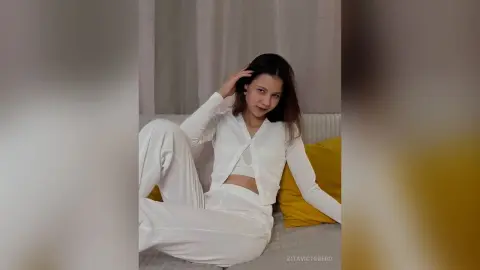 Young woman in white loungewear relaxing on a sofa with a yellow pillow in a bright, cozy room.