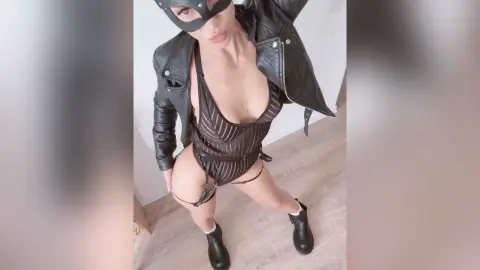Woman in black leather jacket and striped bodysuit posing confidently in a modern indoor setting.