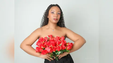 Elegant woman with long braids holding a vibrant red rose bouquet against a clean white background.