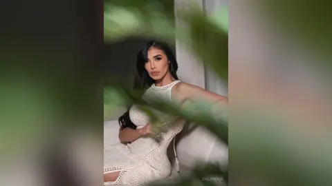 Elegant woman in a white lace cocktail dress sitting in a bright, modern indoor setting.